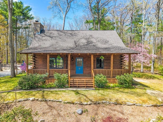 log-style house with a porch, log siding, roof with shingles, and a chimney