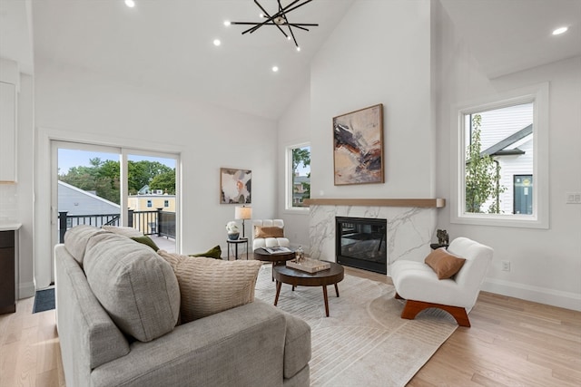 living room with a high end fireplace, high vaulted ceiling, light wood-type flooring, and a wealth of natural light