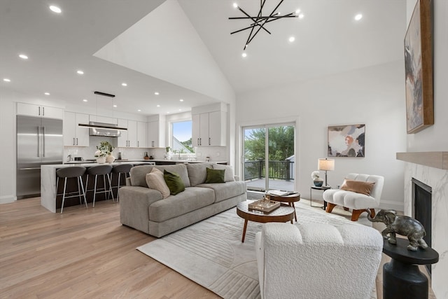 living room featuring high vaulted ceiling, light hardwood / wood-style floors, a high end fireplace, and an inviting chandelier