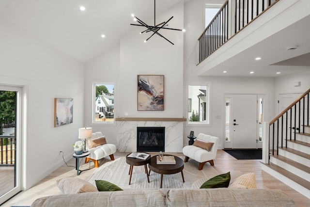 living room with a notable chandelier, light hardwood / wood-style floors, a premium fireplace, and high vaulted ceiling