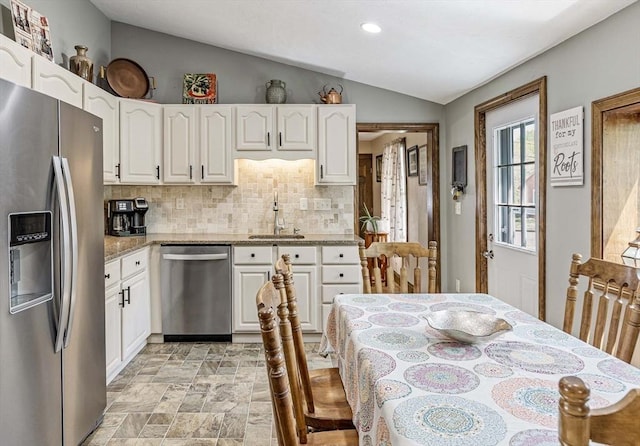 kitchen with light stone countertops, appliances with stainless steel finishes, a sink, decorative backsplash, and vaulted ceiling