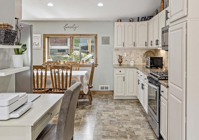 kitchen with stone finish floor, visible vents, stainless steel range with gas stovetop, tasteful backsplash, and white cabinetry