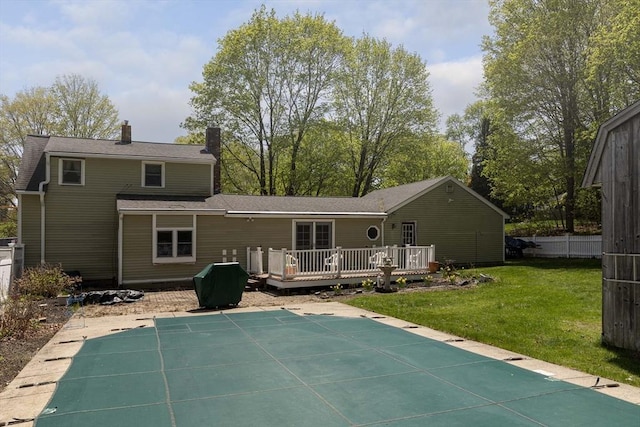 back of house with a lawn, a wooden deck, a covered pool, and a chimney