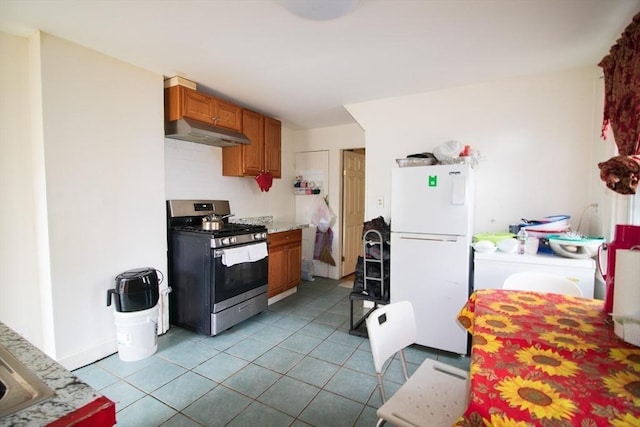 33 Cady St, Lowell, MA 01852 - kitchen featuring freestanding refrigerator, gas range, under cabinet range hood, brown cabinetry, and tile patterned floors