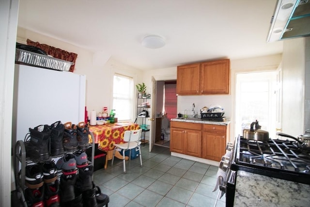 33 Cady St, Lowell, MA 01852 - kitchen with stainless steel gas stove, light tile patterned floors, brown cabinets, a sink, and extractor fan