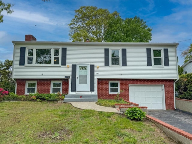 bi-level home featuring a garage, asphalt driveway, brick siding, and a chimney