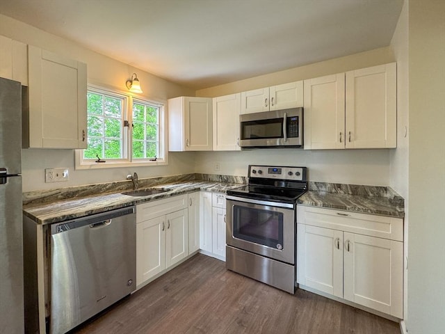 kitchen featuring appliances with stainless steel finishes, a sink, white cabinetry, dark wood-type flooring, and dark countertops