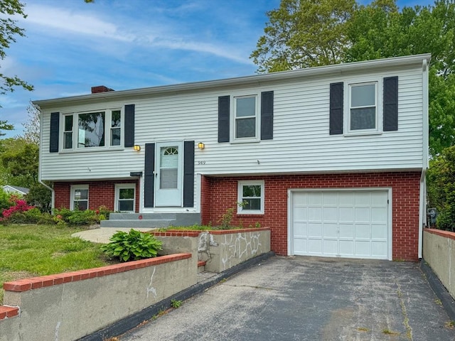 bi-level home with brick siding, an attached garage, asphalt driveway, and a chimney