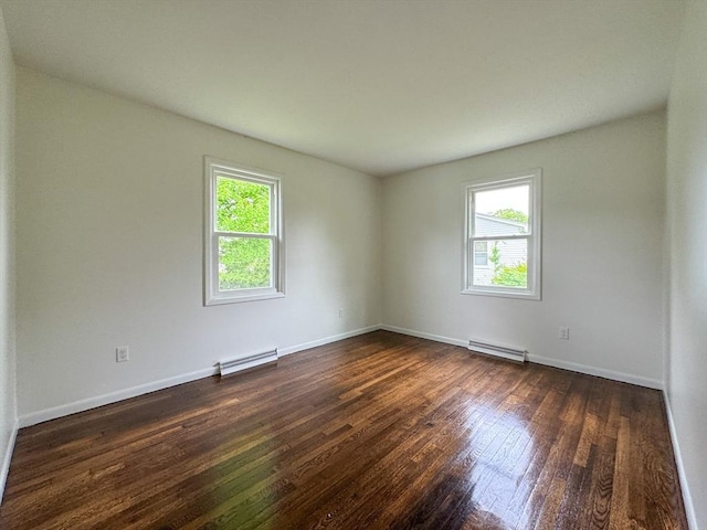 spare room featuring healthy amount of natural light, dark wood-type flooring, a baseboard heating unit, and baseboards