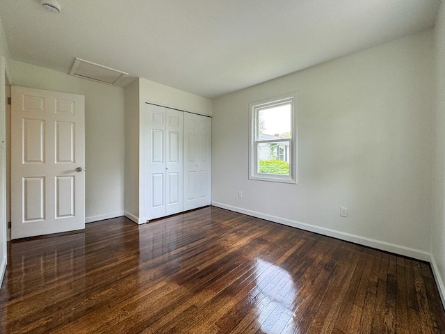 unfurnished bedroom featuring attic access, dark wood-style floors, and baseboards