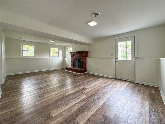 unfurnished living room featuring wood finished floors, a brick fireplace, a wainscoted wall, and baseboards