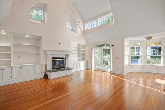 unfurnished living room with a high ceiling, built in features, and light hardwood / wood-style floors