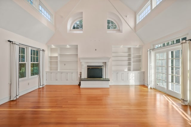 unfurnished living room featuring built in features, high vaulted ceiling, and light hardwood / wood-style flooring