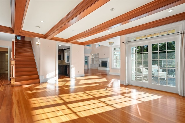 unfurnished living room with ornamental molding, light wood-type flooring, and beam ceiling