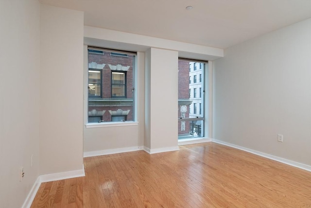 unfurnished room featuring a healthy amount of sunlight, light wood-style flooring, and baseboards