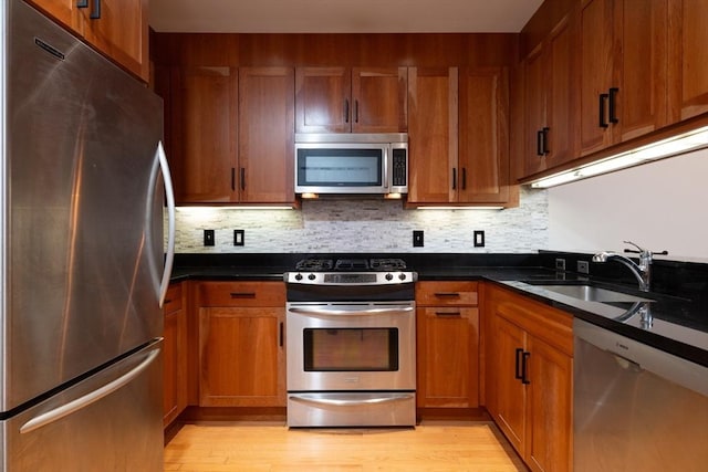 kitchen with appliances with stainless steel finishes, dark countertops, a sink, and brown cabinets