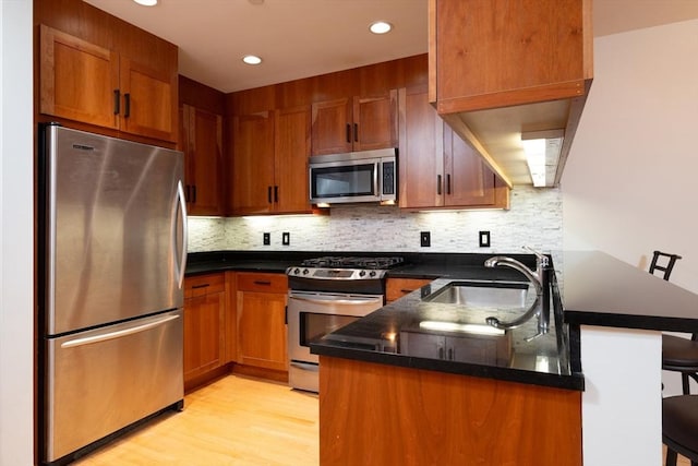 kitchen featuring a breakfast bar, backsplash, appliances with stainless steel finishes, a sink, and a peninsula