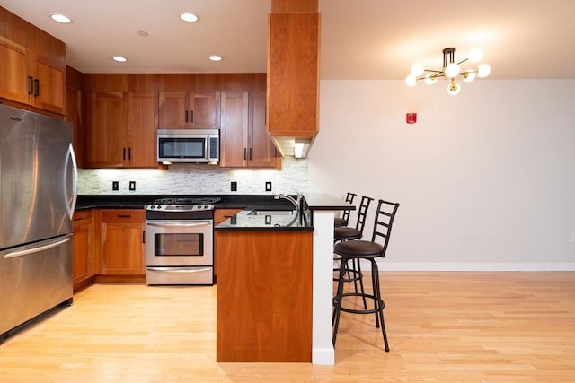 kitchen featuring a breakfast bar, a sink, appliances with stainless steel finishes, tasteful backsplash, and dark countertops