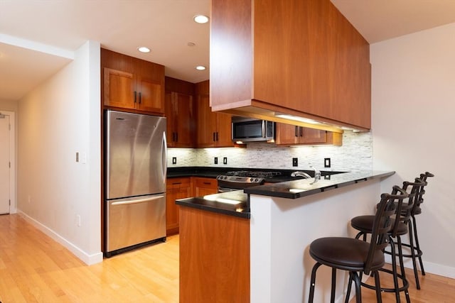 kitchen with stainless steel appliances, backsplash, brown cabinetry, a peninsula, and a kitchen bar