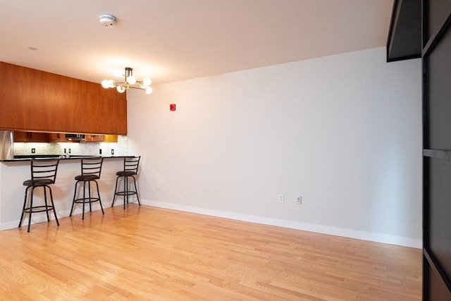 kitchen featuring light wood-style flooring, a notable chandelier, a breakfast bar, decorative backsplash, and brown cabinetry