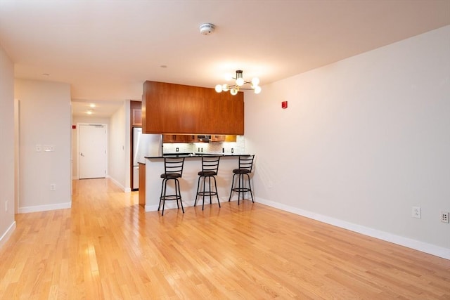 kitchen featuring brown cabinets, light wood-style floors, a chandelier, a peninsula, and a kitchen bar