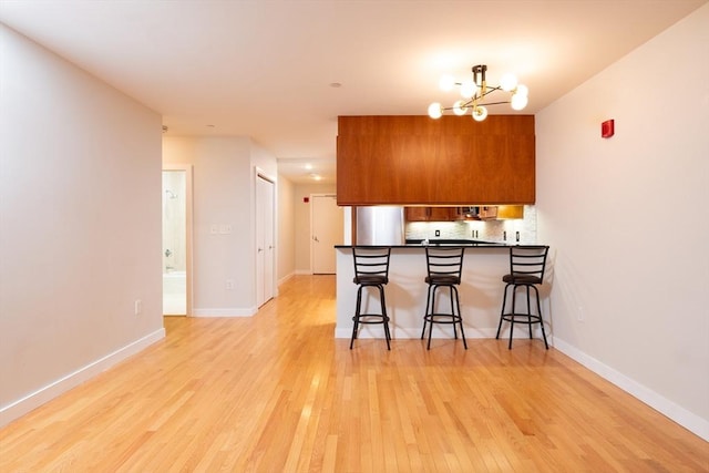 kitchen with light wood-type flooring, brown cabinetry, decorative backsplash, and a kitchen breakfast bar