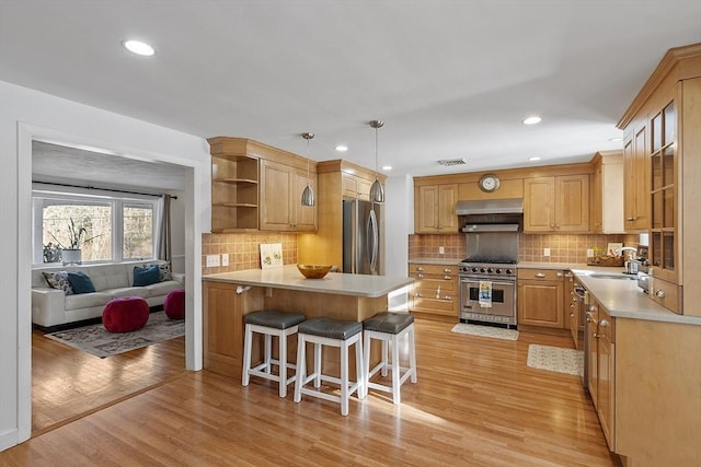 kitchen featuring appliances with stainless steel finishes, sink, backsplash, a kitchen bar, and light wood-type flooring