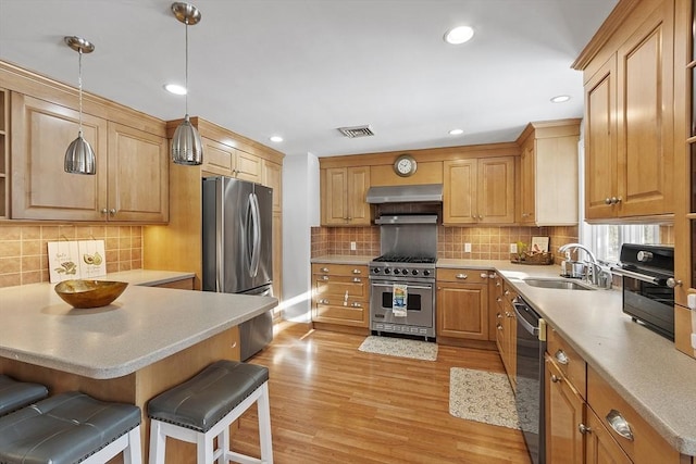 kitchen featuring sink, decorative light fixtures, light wood-type flooring, appliances with stainless steel finishes, and a kitchen breakfast bar