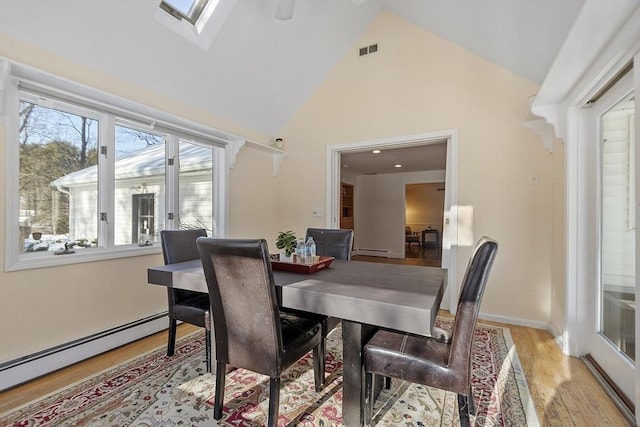 dining room featuring a baseboard heating unit, a skylight, high vaulted ceiling, and light wood-type flooring