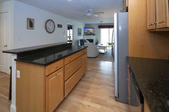 kitchen featuring light wood finished floors, a ceiling fan, a kitchen island, freestanding refrigerator, and a fireplace