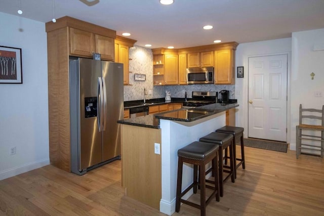 kitchen featuring light wood finished floors, tasteful backsplash, a kitchen bar, and appliances with stainless steel finishes