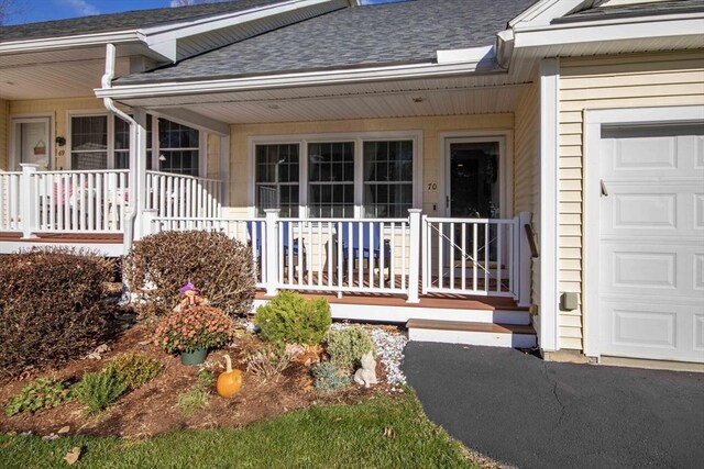 view of exterior entry with a shingled roof, covered porch, and an attached garage