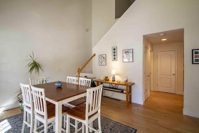 dining area featuring stairs, wood finished floors, a towering ceiling, and baseboards