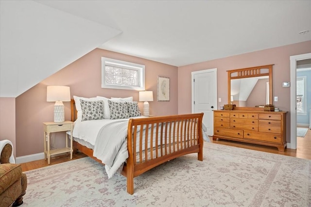 bedroom with vaulted ceiling, wood finished floors, and baseboards