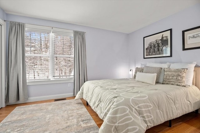 bedroom featuring wood finished floors, visible vents, baseboards, and multiple windows