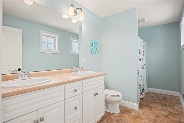 bathroom featuring double vanity, a sink, toilet, and baseboards