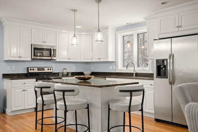 kitchen with stainless steel appliances, dark countertops, a kitchen bar, and white cabinetry