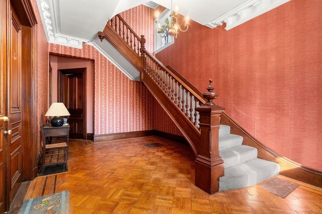 stairs with a notable chandelier, crown molding, and parquet flooring