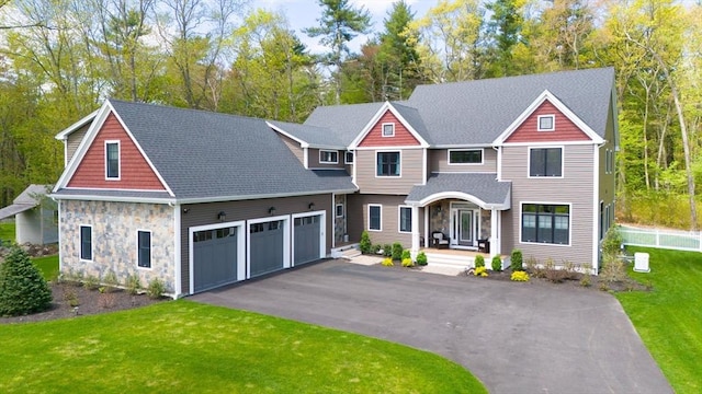 view of front of home featuring aphalt driveway, a garage, stone siding, roof with shingles, and a front yard