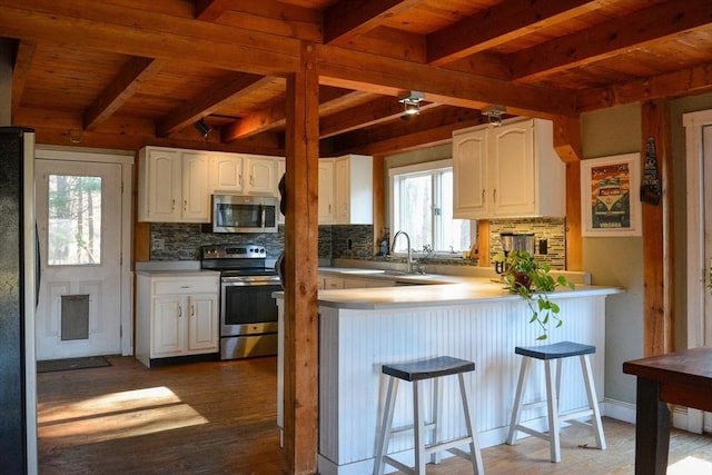 kitchen featuring decorative backsplash, kitchen peninsula, stainless steel appliances, white cabinets, and a breakfast bar area