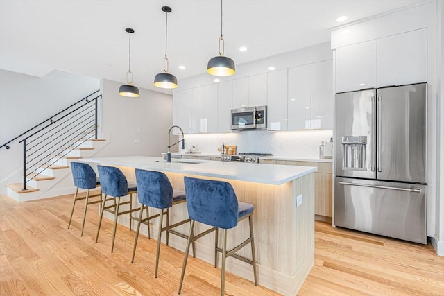 kitchen with a kitchen island with sink, white cabinets, sink, light hardwood / wood-style flooring, and appliances with stainless steel finishes