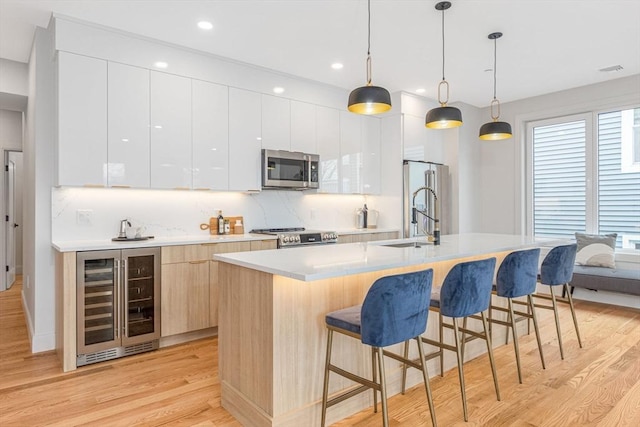 kitchen with appliances with stainless steel finishes, hanging light fixtures, a kitchen island with sink, and wine cooler