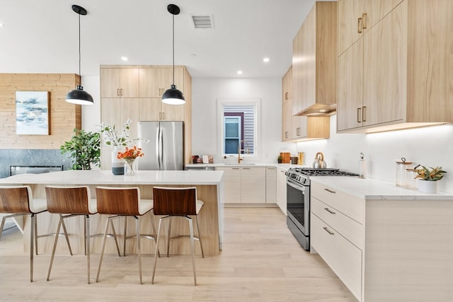 kitchen with light brown cabinetry, hanging light fixtures, appliances with stainless steel finishes, and light hardwood / wood-style flooring