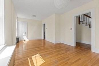 unfurnished room with light wood-type flooring, baseboards, and stairs