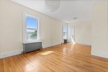 unfurnished room with baseboards, radiator, and wood finished floors