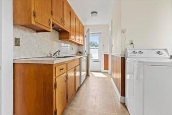 kitchen with a sink, light countertops, dishwashing machine, brown cabinets, and washer / dryer