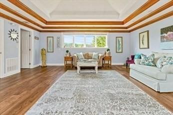 living room with a raised ceiling, wood finished floors, baseboards, and ornamental molding