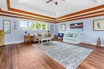 living room with ceiling fan, a raised ceiling, wood finished floors, and baseboards