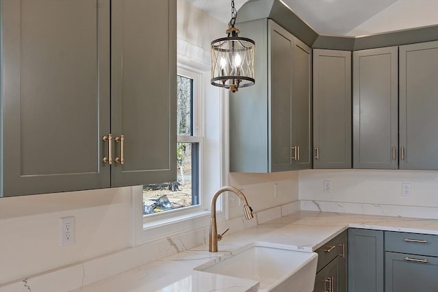 kitchen featuring a sink, gray cabinets, light stone counters, pendant lighting, and an inviting chandelier