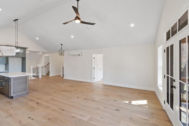 unfurnished living room featuring light wood finished floors, ceiling fan with notable chandelier, a wall unit AC, high vaulted ceiling, and baseboards